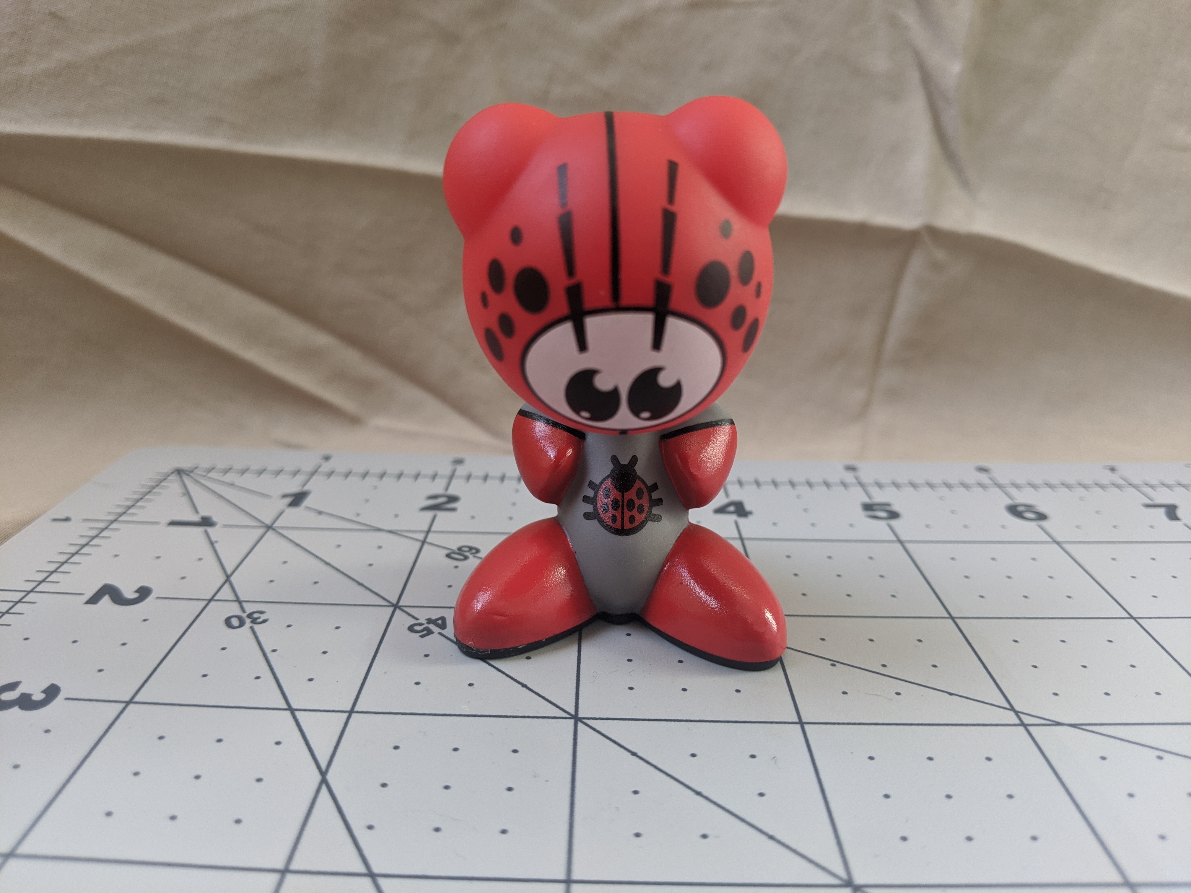 A red Funkey on top of measuring paper. It is a red humanoid form.